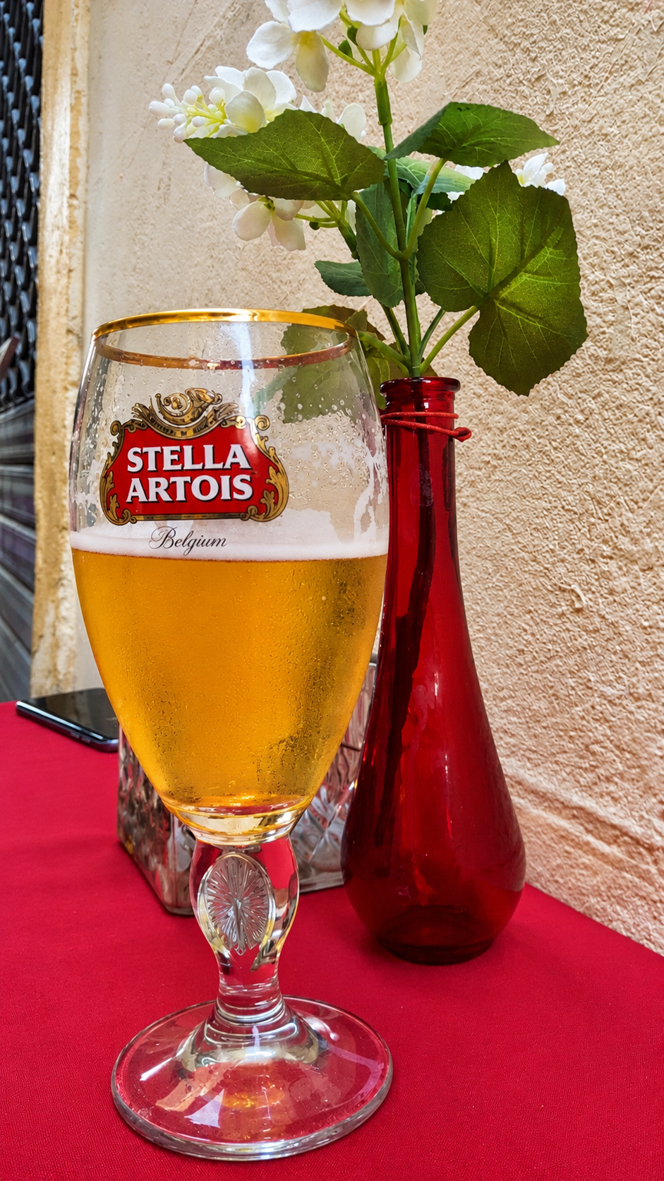 Cold Stella Artois beer beside a red vase of white flowers at a table in Arles